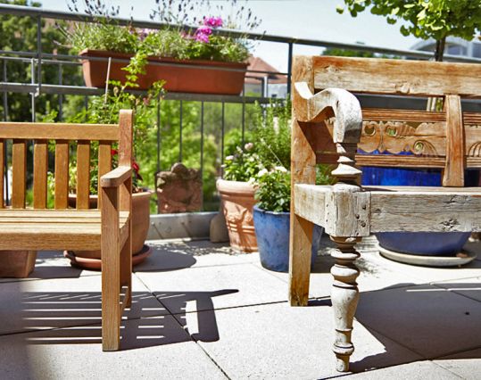 Blick vom Therapiezimmer aus auf die Terrasse mit Holzbank und Blumenkübeln in der Sonne