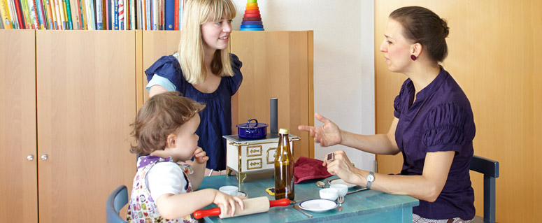 Elternberatung: Mutter im Gespräch mit Christine Moritz, während Tochter mit Kochutensilien am Tisch spielt